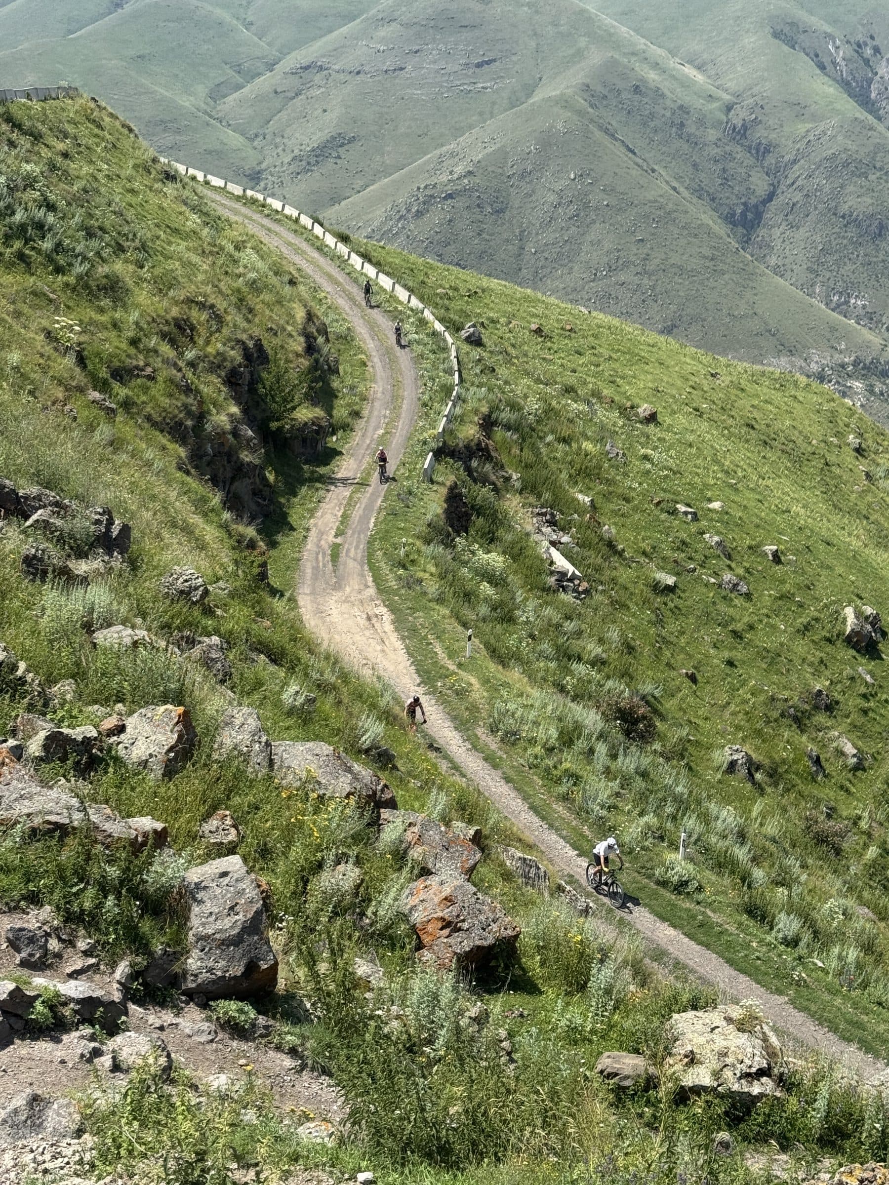 Riders spread along a gravel switchback climbing high into the green Caucasus mountains