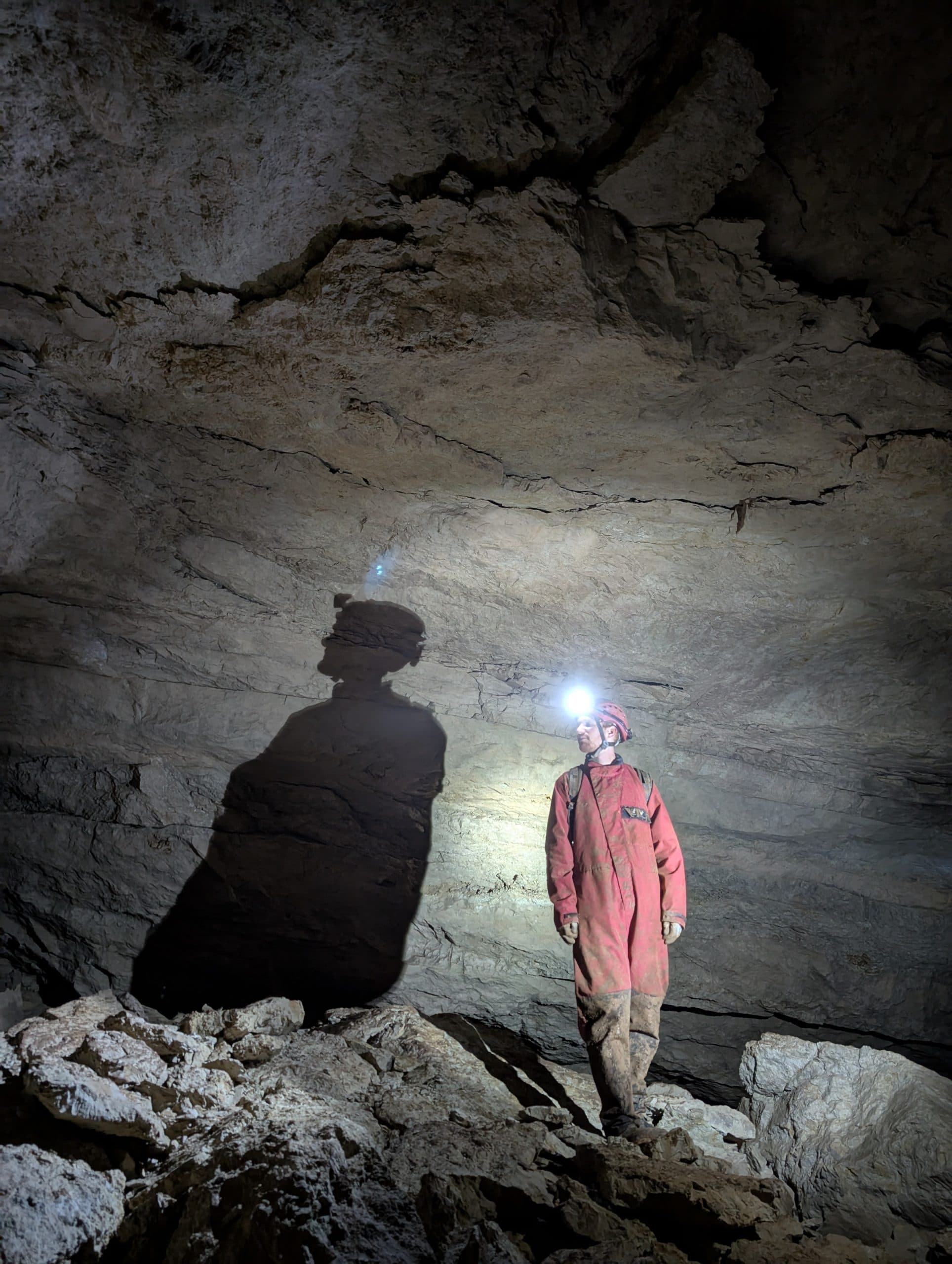 A caver and their long shadow in a lamplit cave chamber