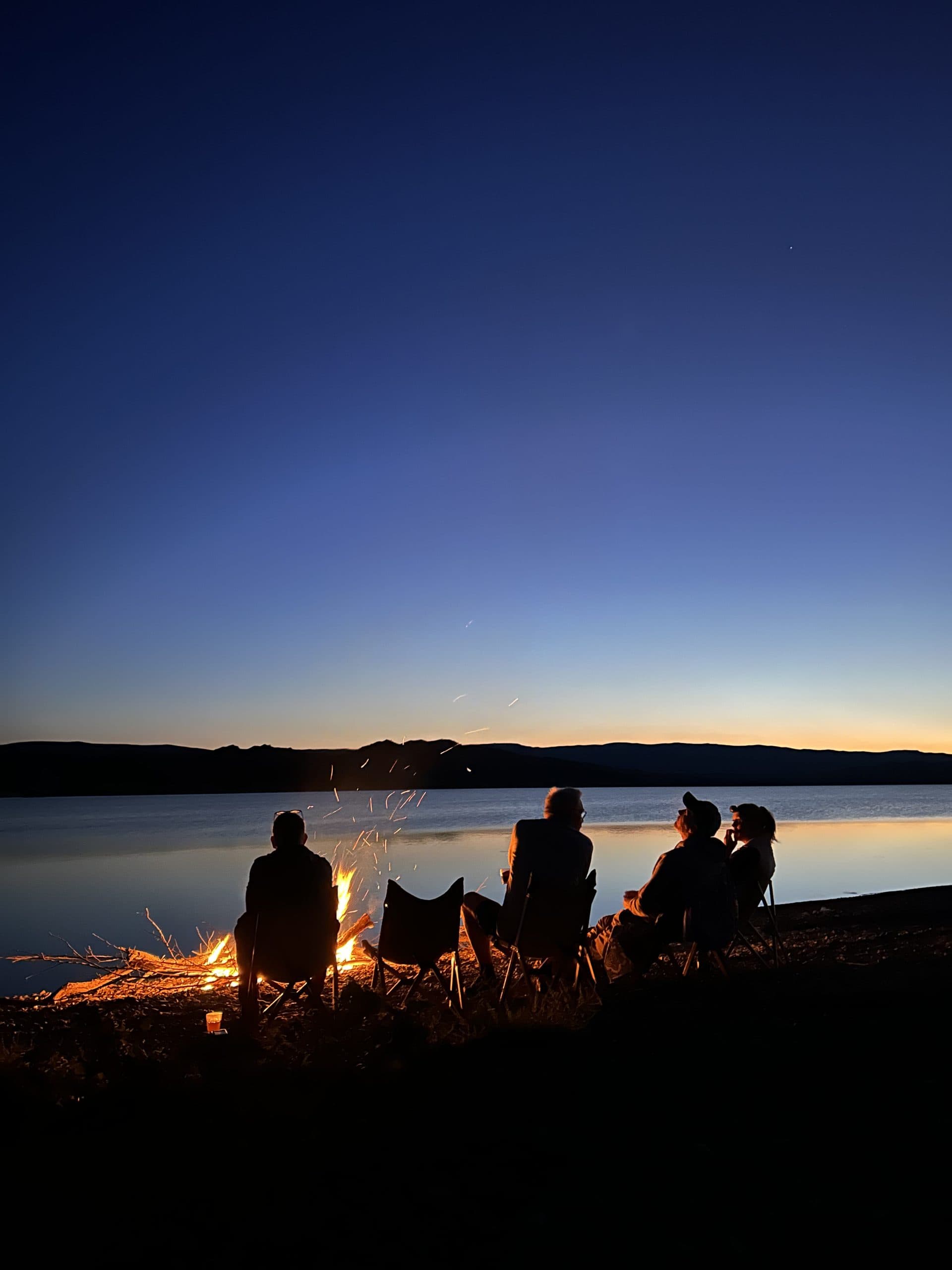 Travellers around a campfire beside a mountain lake at dusk