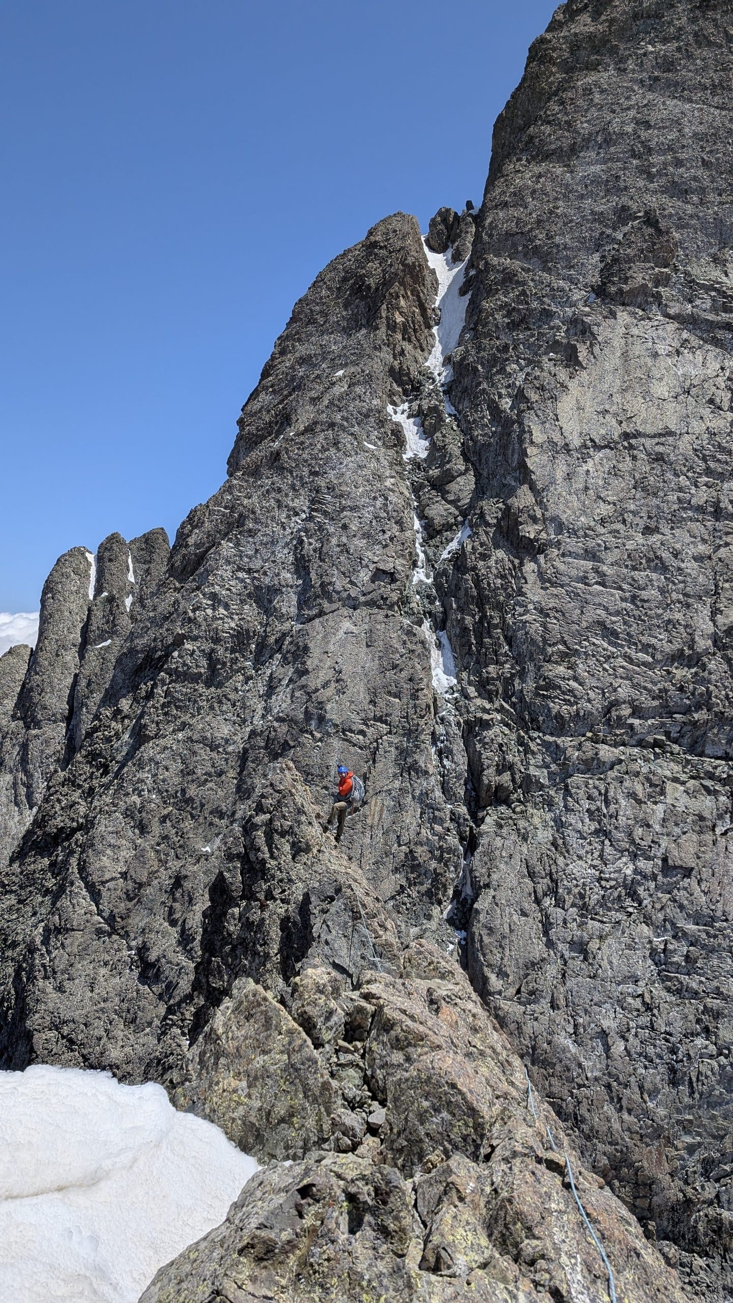 A climber on a sharp Chaukhi spire above a snow couloir